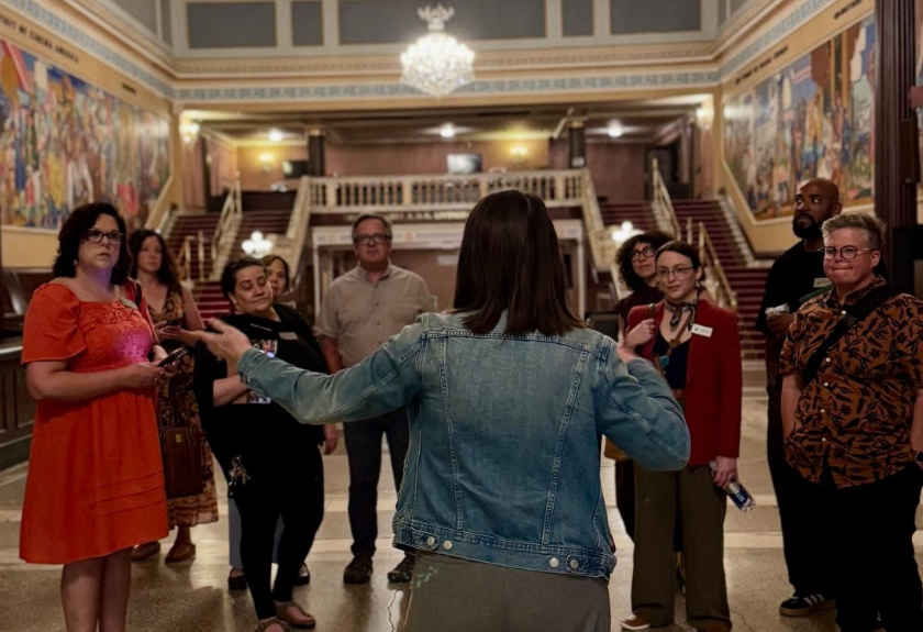 A person speaks to a group gathered inside a grand building