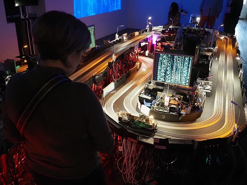 A person in the foreground looks at a digital art installation that resembles an electric toy race track