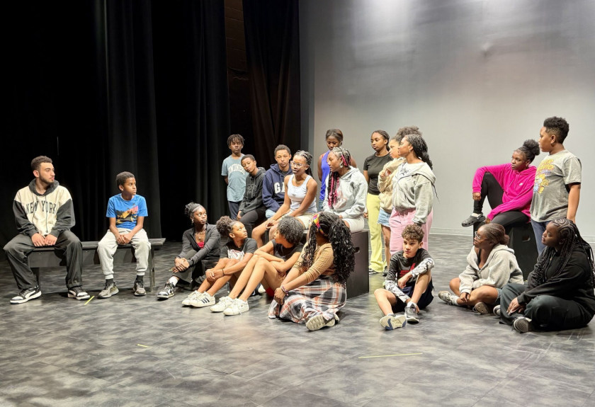 A diverse group of youth sitting on a stage listening to a man speak.