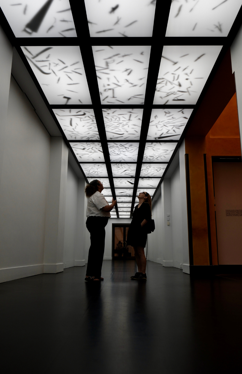 Two people stand under a patterned, backlit ceiling in a modern hallway