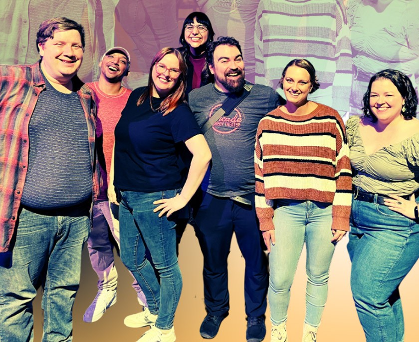 Seven laughing people stand in a row posing for the camera