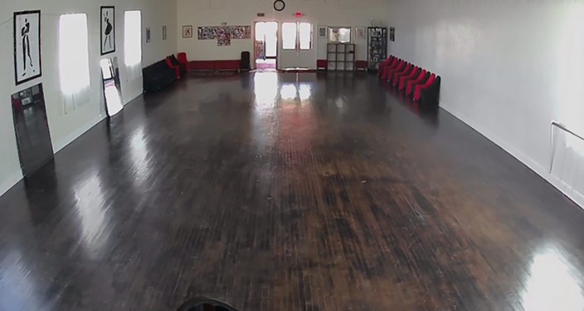 A security camera view of an empty studio with dark wooden floors and artwork hanging on the walls