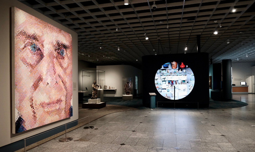 Museum gallery with a large mosaic portrait and a circular display of various objects on the wall.