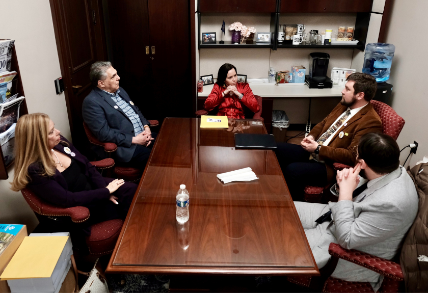 Five people sit around a conference table in an office, having a discussion.