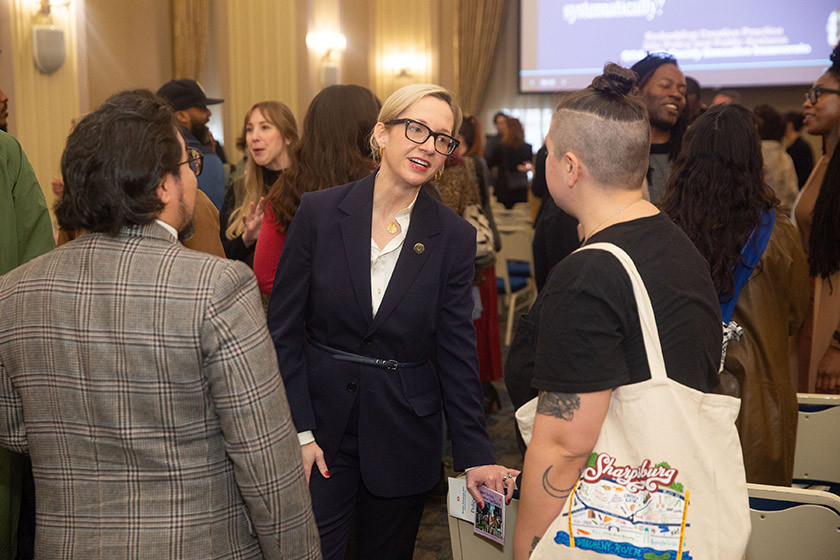 People conversing in a conference room with chairs and a presentation screen.