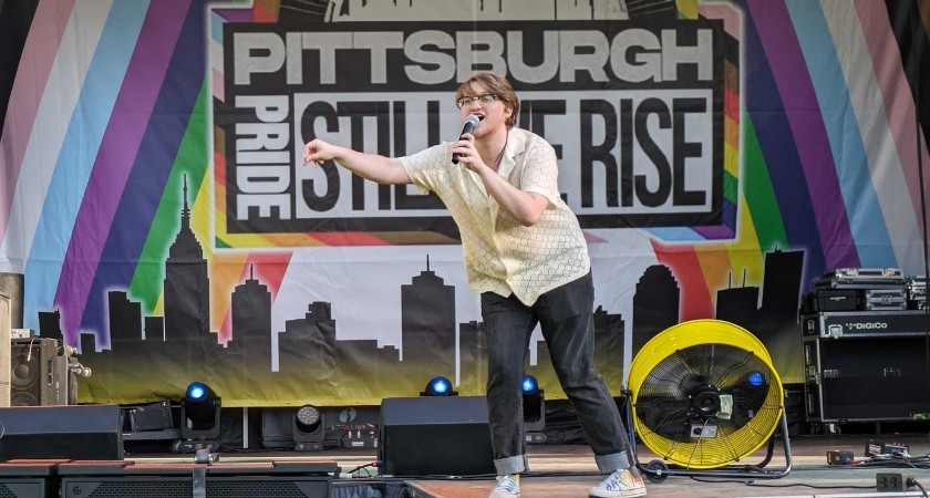A white person on stage in front of a sign that says pittsburgh pride still we rise