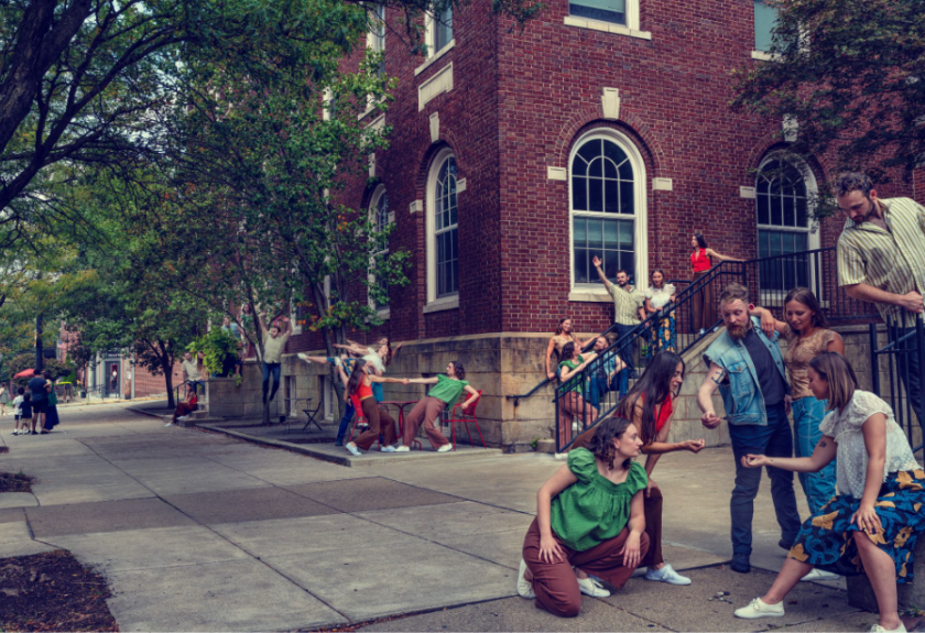 A group of people interact on a sidewalk and stairs outside a red brick building