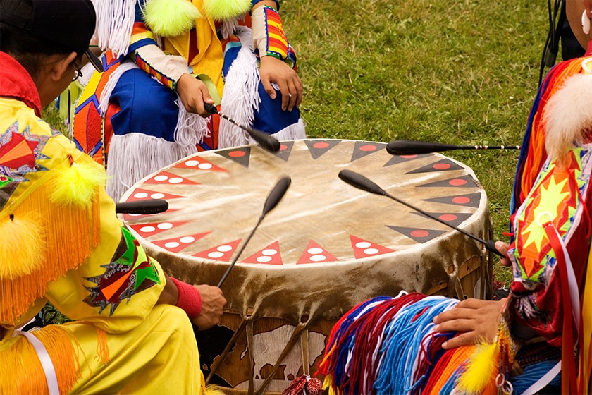 A group of Native Americans sit in a circle around a drum