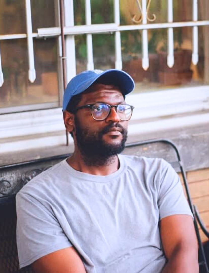 Man wearing glasses and a blue cap sitting on a bench by a window.