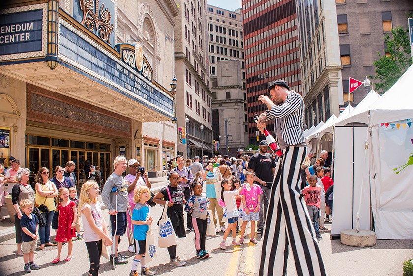 Man on stilts wearing a black-and-white striped suit juggles in front of a crowd of families and children 