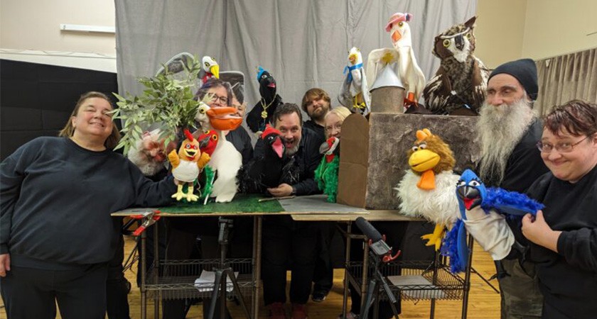 A group of people gathered around a card table holding up various animal puppets
