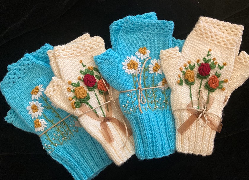 Four pairs of gloves embroidered with floral patterns. Two gloves are blue and two are tan