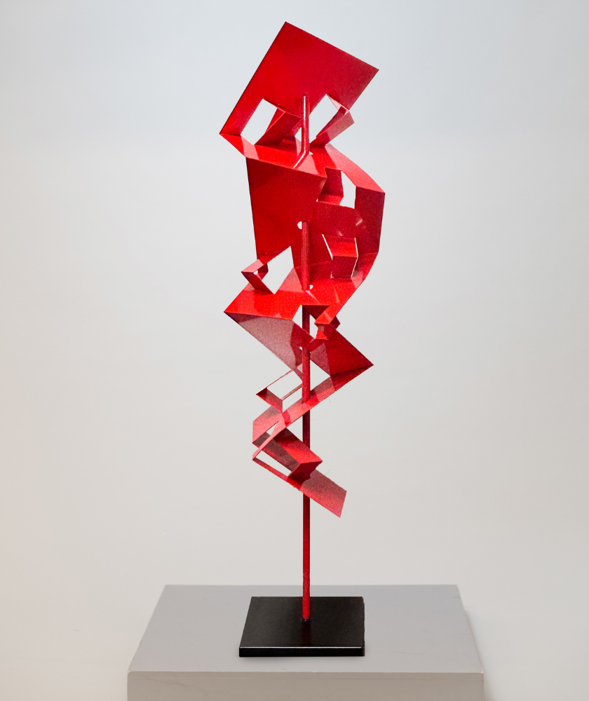 A modern abstract sculpture made of red geometric metal shapes stacked asymmetrically on a vertical rod, displayed on a black and gray pedestal against a plain white background.