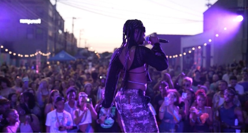 A black man standing on a stage with a microphone with a crowd below him 