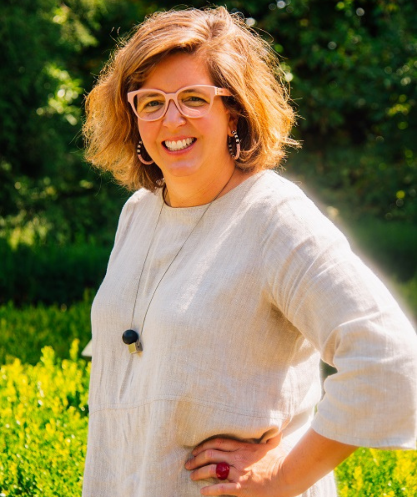 Woman with short hair and glasses smiling outdoors in sunlight