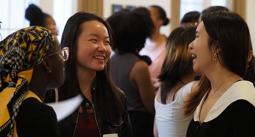Three people stand laughing in the foreground as a large crowd gathers in the background