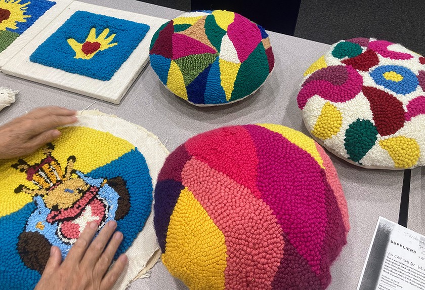 A person's hands are shown working on a colorful textile work