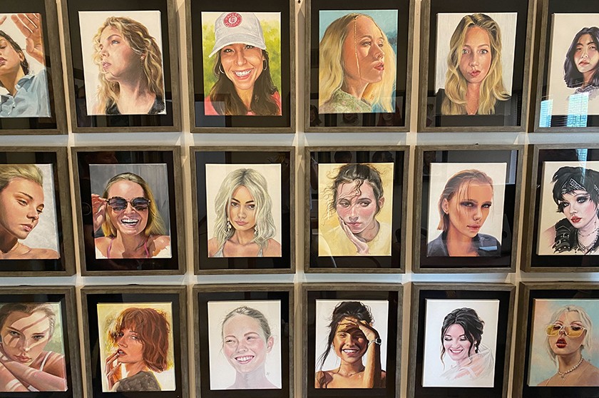 A photograph showing 18 framed acrylic portrait paintings hanging on a wall