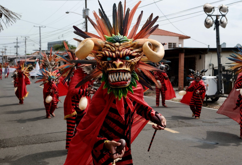 People in colorful demon masks and costumes parade down a street during a festival.