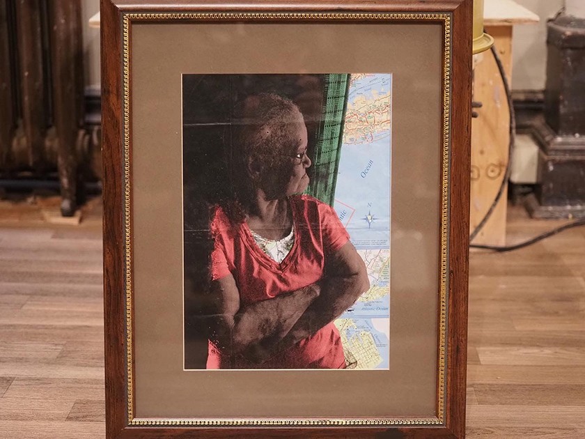 Framed artwork of a Black woman with her arms crossed looking out a window that displays a world map instead of a typical exterior view