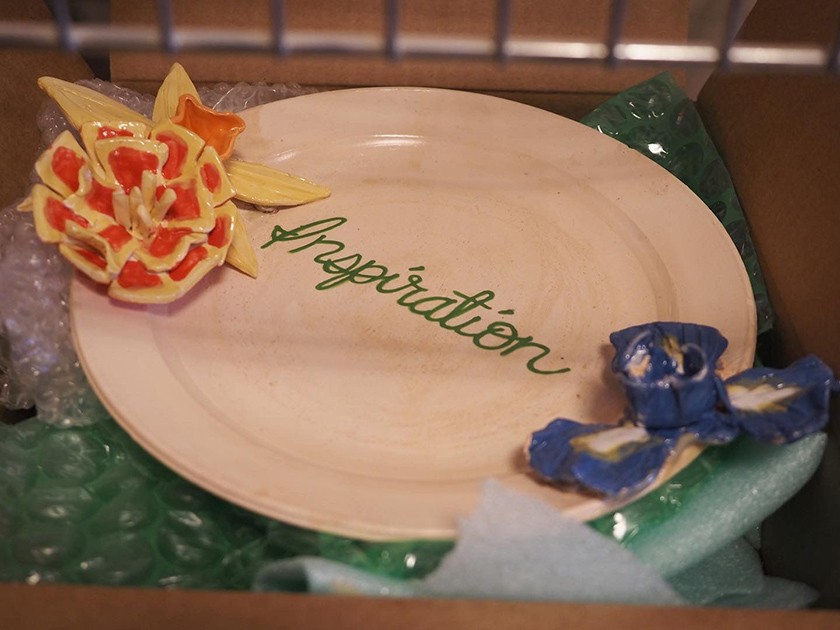 A ceramic plate with a 3D ceramic flower at each end bookending the word "inspiration" written in cursive