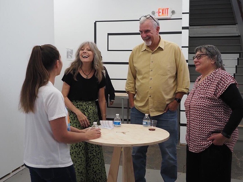 A group of four people stand laughing and talking around a table