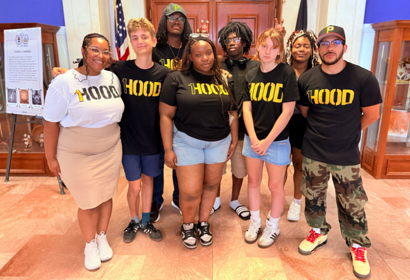 A group of eight people wearing shirts labeled HOOD standing together indoors.