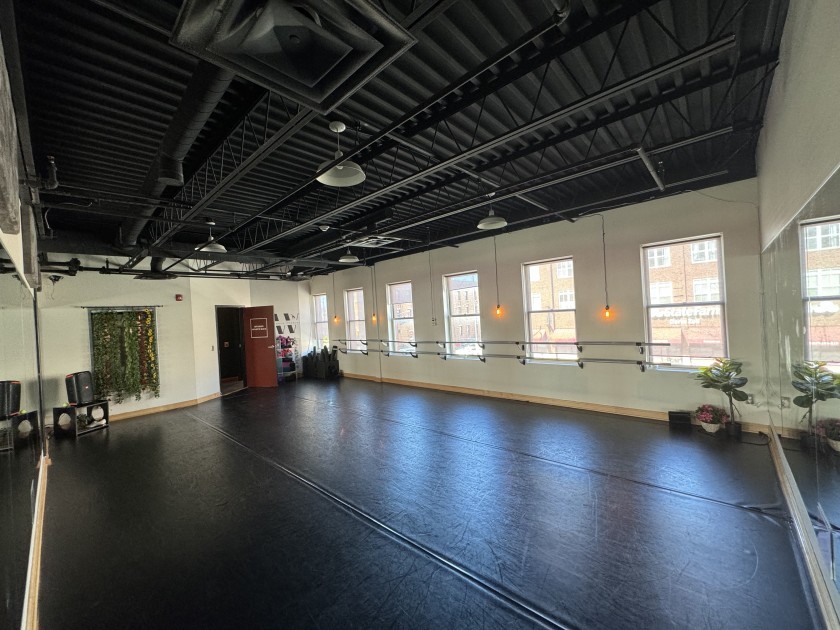 A spacious empty studio space with a dark floor and large windows