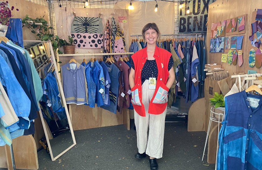 Smiling woman poses in front of a display of upcycled clothing