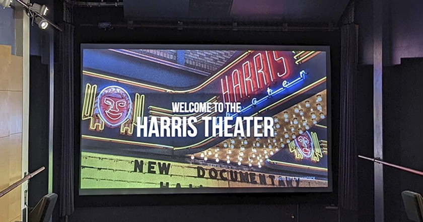 The interior of a movie theater with the screen reading, "Welcome to the Harris Theater," typed on top of a photo of the exterior movie marquee