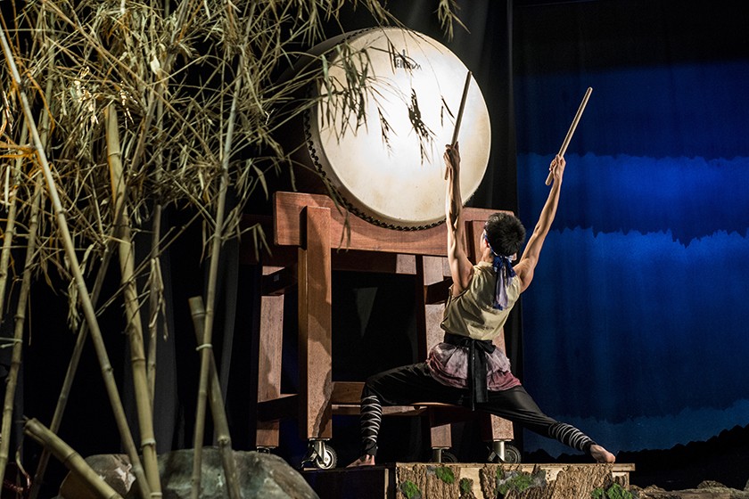 An Asian person is shown from behind as they're holding up drum sticks in front of an oversized drum