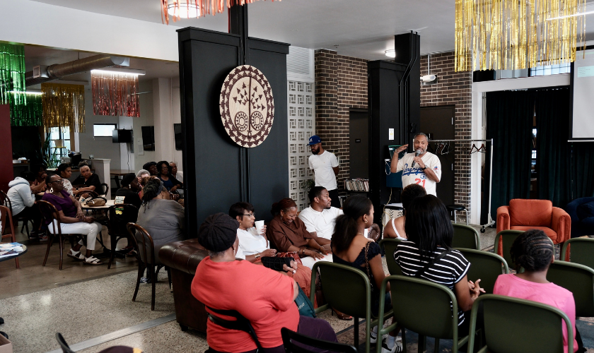 People sit and listen to a speaker in a cozy, decorated community room with colorful streamers.