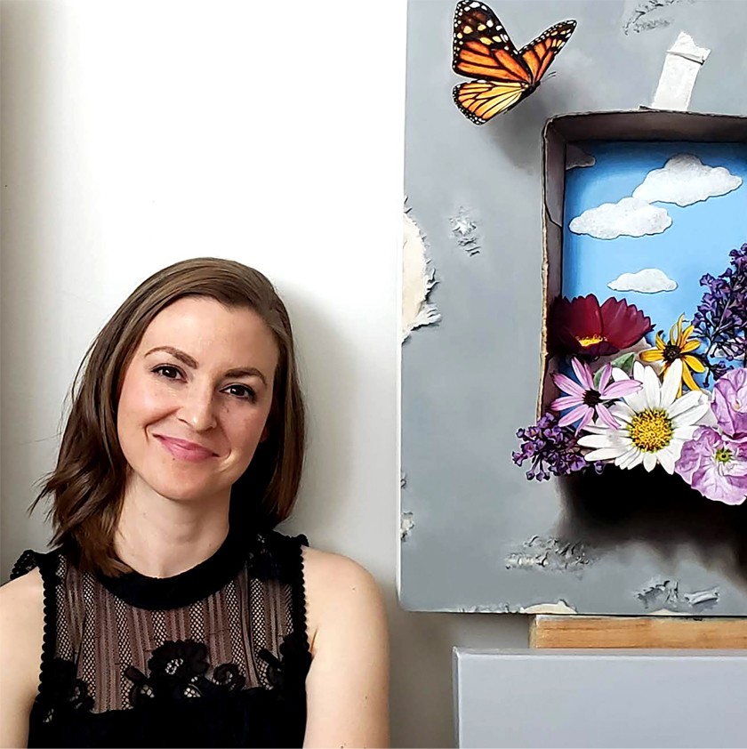 A smiling white woman with shoulder-length brown hair standing next to an acrylic painting of flowers and butterflies