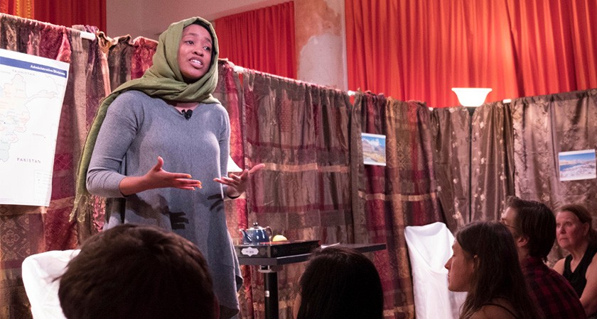 A woman with her head covered in a green scarf speaks before a crowd in a bookstore