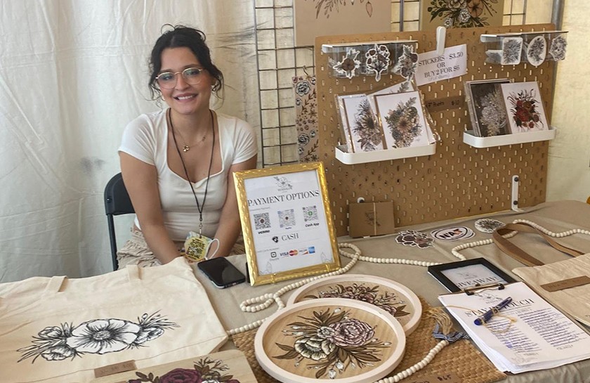 Smiling woman with brunette hair, sitting at a booth surrounded by artwork