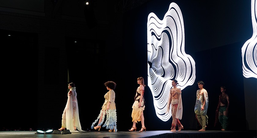 A group of models in white outfits walking down a runway