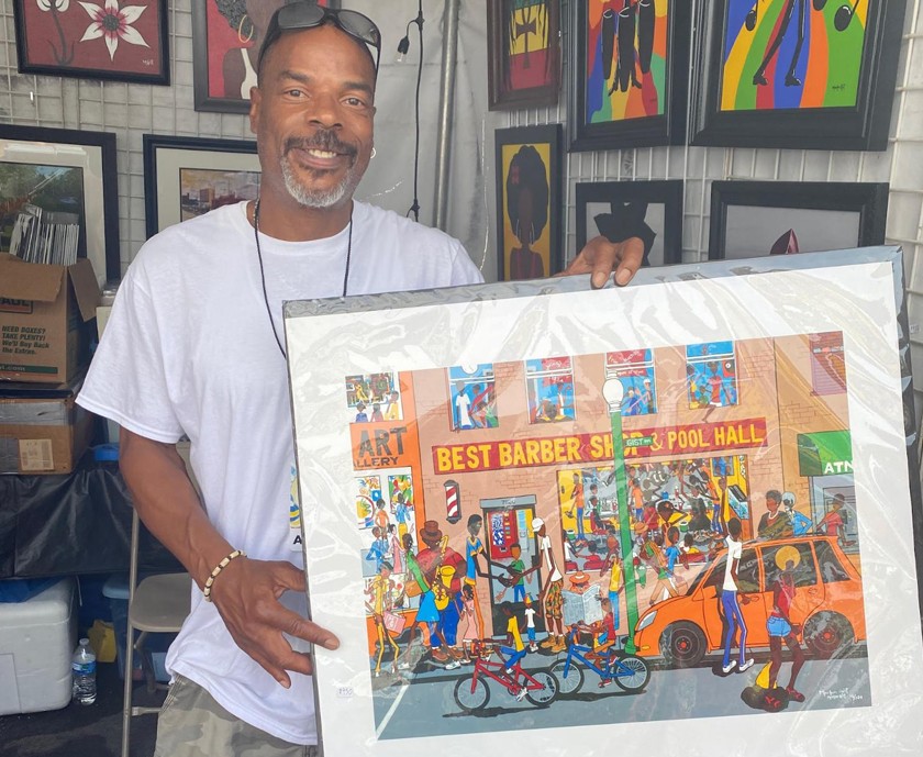 Smiling Black man holding a piece of artwork in a booth at an arts festival