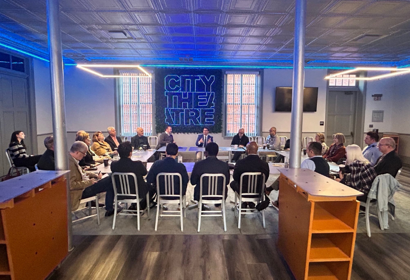 People sit in a circle having a meeting in a room with a City Theatre sign on the wall.