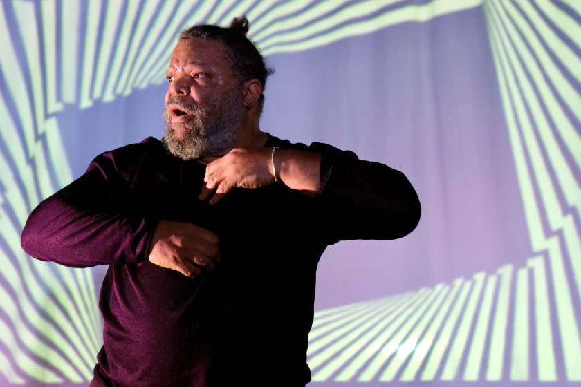 A performer mid-movement on stage against a backdrop of bold geometric projections