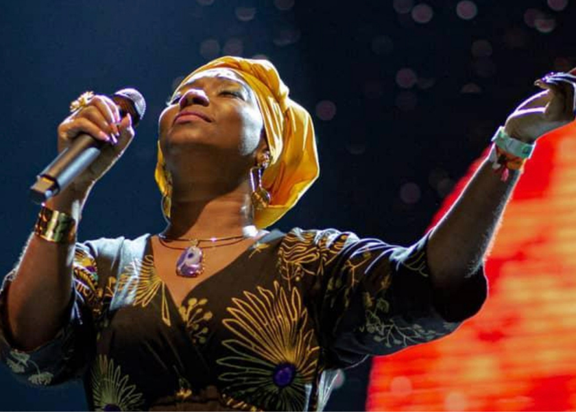 A woman in a yellow headwrap sings passionately on stage