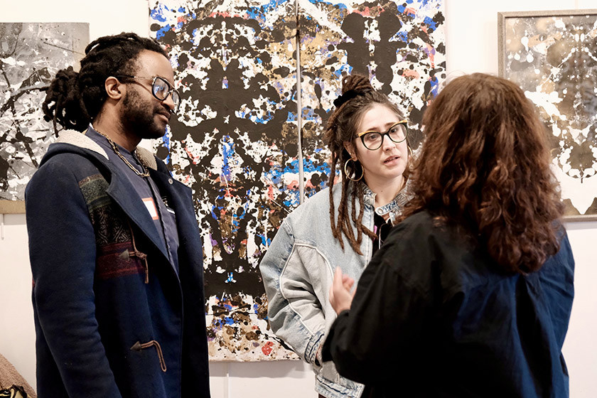 Three people talk inside an arts gallery