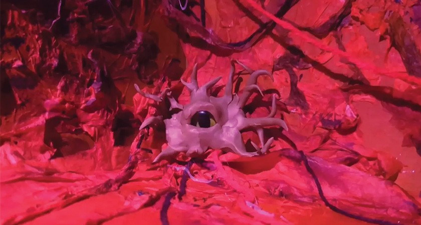 A pink amoeba-like creature with a human eye ball is shown on top of a dark fuscia-tinted textured background