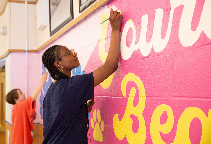 Two people painting large, colorful letters on a wall mural