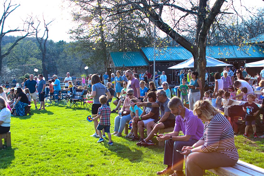 A large group of adults and children gather in a park on a sunny day