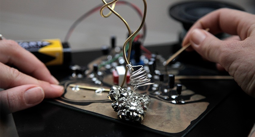 Close-up photo of hands working on an unidentified object with lots of buttons and wires