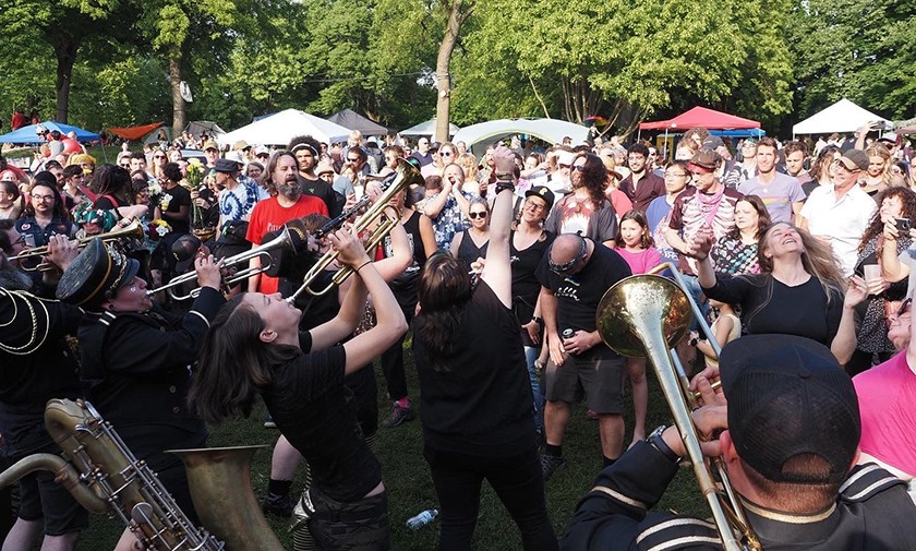 A large crowd watches brass musicians playing at an outside festival