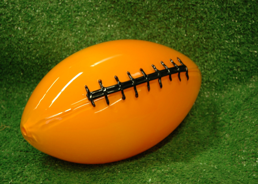 An orange glass football on green artificial turf