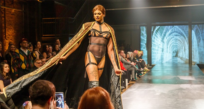 A person in a corset and a cape walks a fashion runway