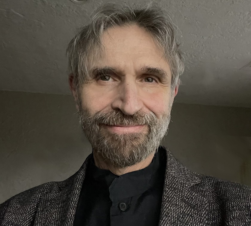 A white man with a goatee and short grayish brown hair wearing a black shirt and a gray jacket