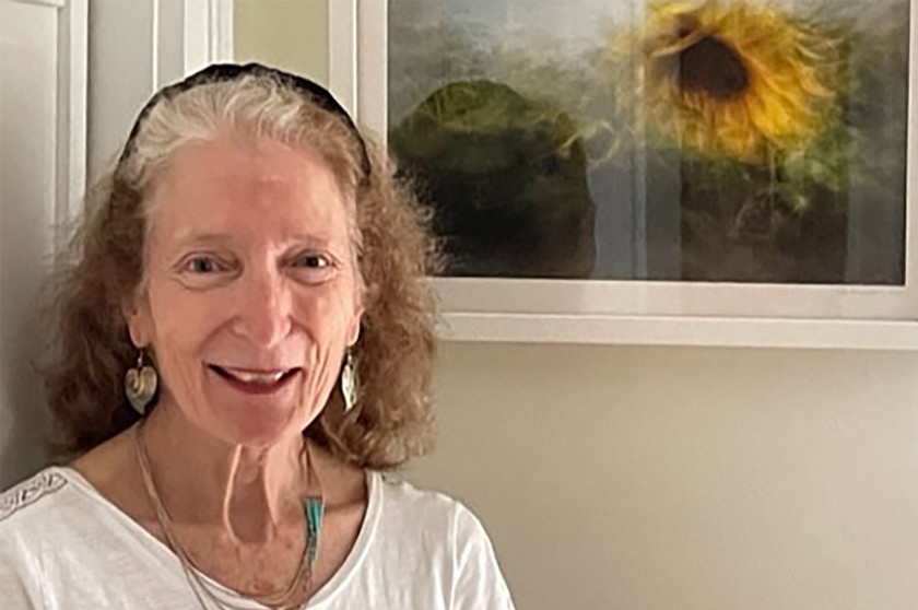 A smiling white woman stands in front of sunflower artwork framed on a wall